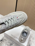 Light gray sneakers close-up with lace eyelets, side stripes, and Moncler details
