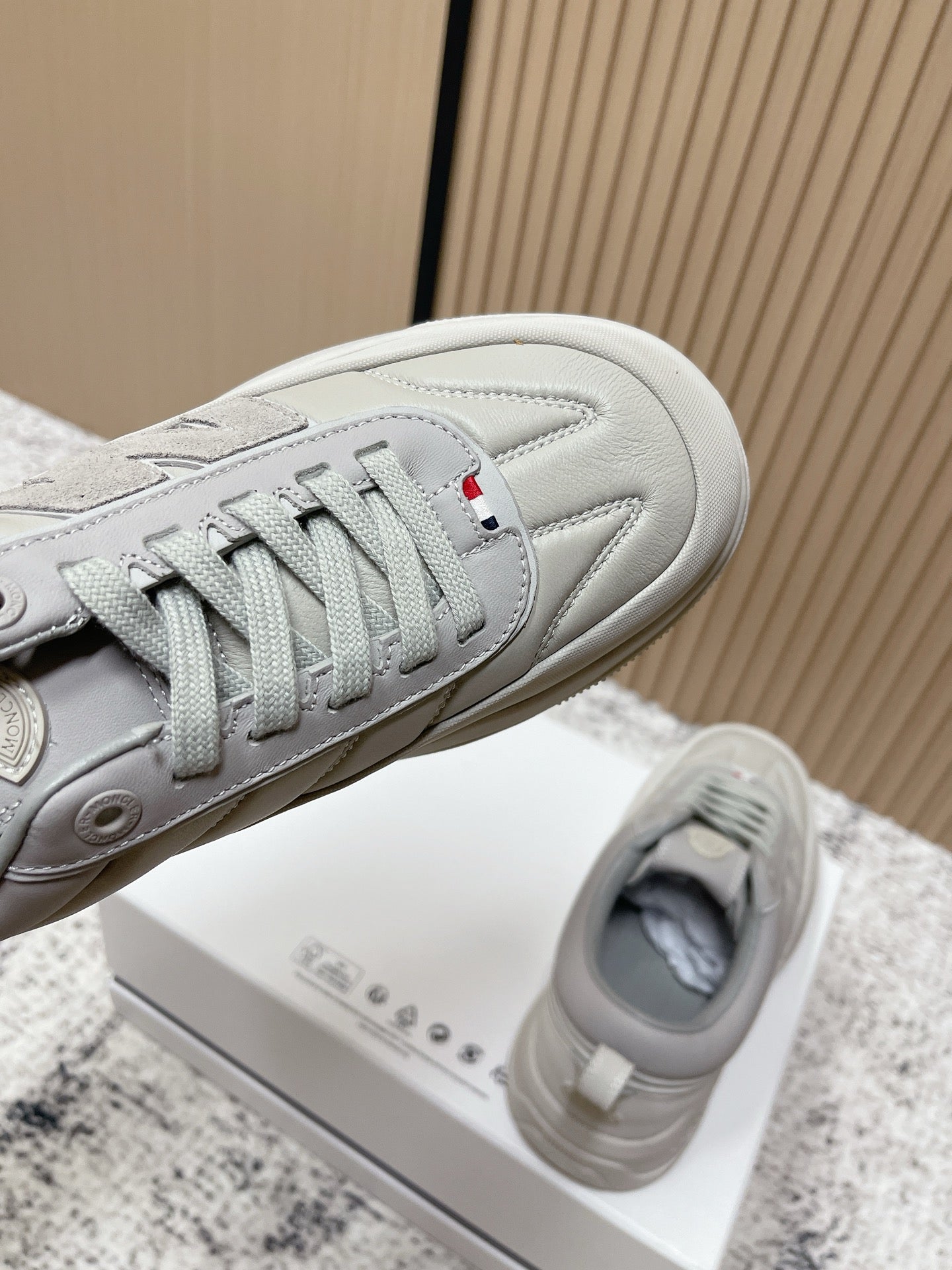 Light gray sneakers close-up with lace eyelets, side stripes, and Moncler details