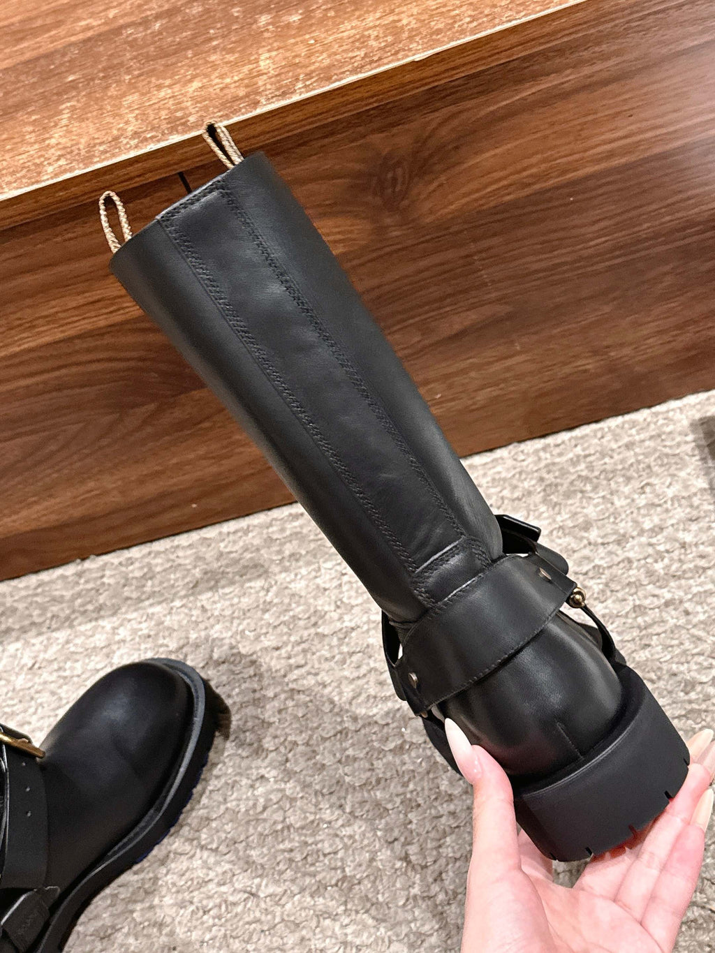 Black mid-calf leather boot with adjustable buckle strap, held in hand.