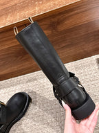 Black mid-calf leather boot with adjustable buckle strap, held in hand.