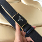 Prada leather belt close-up: black textured strap with gold-toned buckle logo plaque