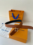 Tan leather belt with dark navy star buckle, placed on a Louis Vuitton shopping box