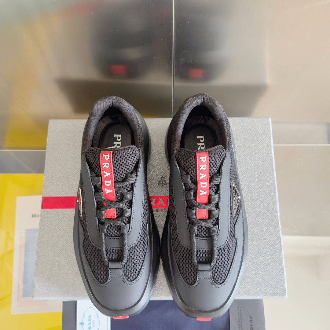 Prada unisex sneakers, front view: dark gray upper with red PRADA tongue straps