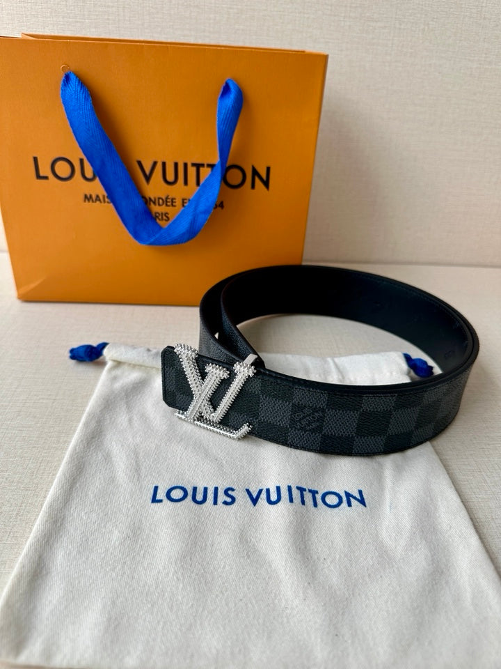 Belt with dark checkered strap and silver-toned LV buckle, resting on a white dust bag
