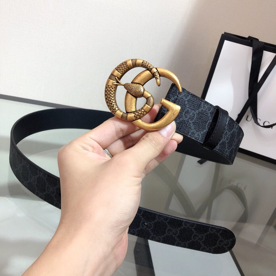 Gucci belt with gold buckle on dark monogram strap, held in hand