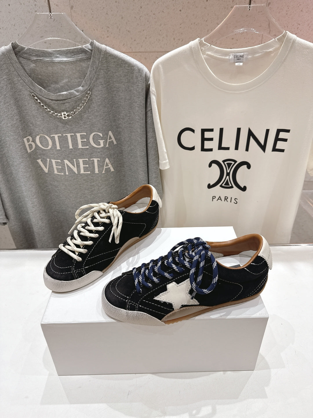 Black and off-white lace-up low-top sneakers set, shown from the front on display boxes.