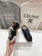 Hand holding a black and off-white low-top sneaker with white laces; pair on display.