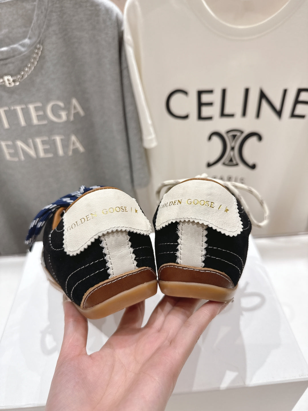 Hand holding two low-top sneakers, showing the heel patch and black/white color blocks.