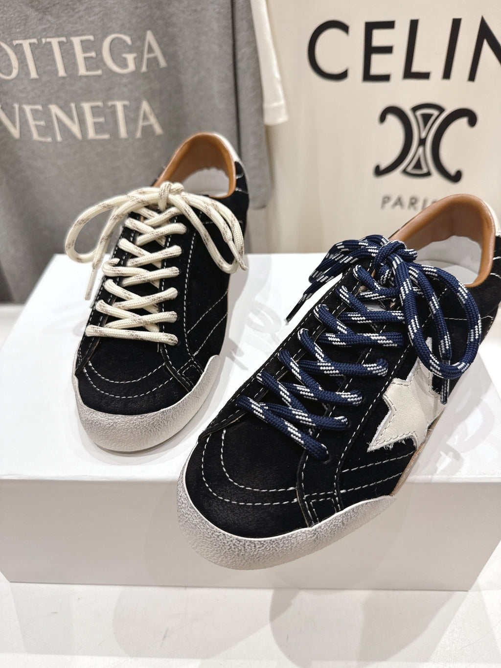 Front view of black and off-white low-top sneakers with white and navy laces on display.
