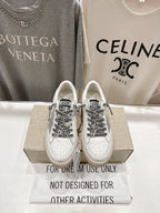 White low-top sneakers with black graphic laces and perforated toe