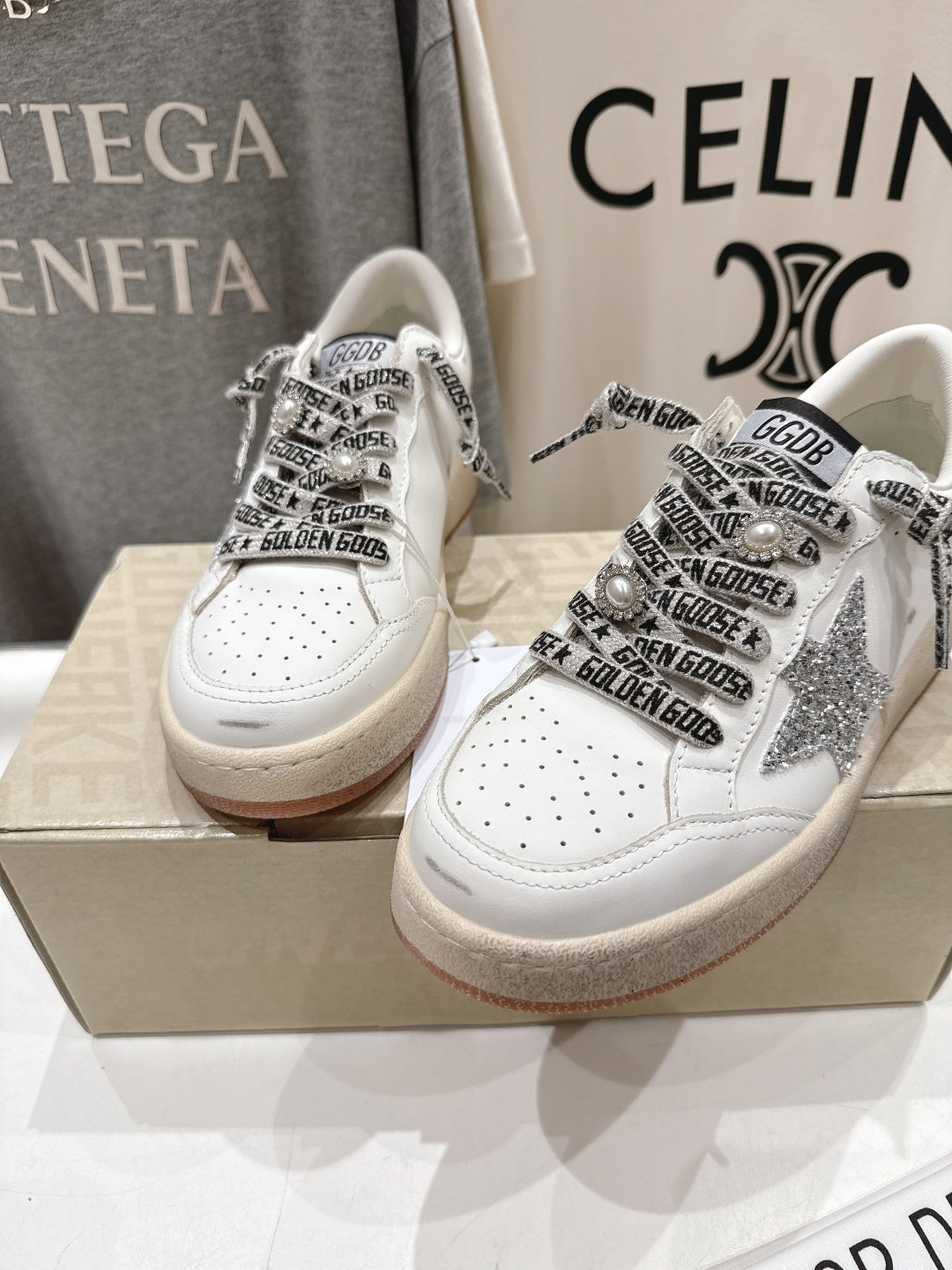 Pair of white low-top sneakers with black graphic laces and perforated toe