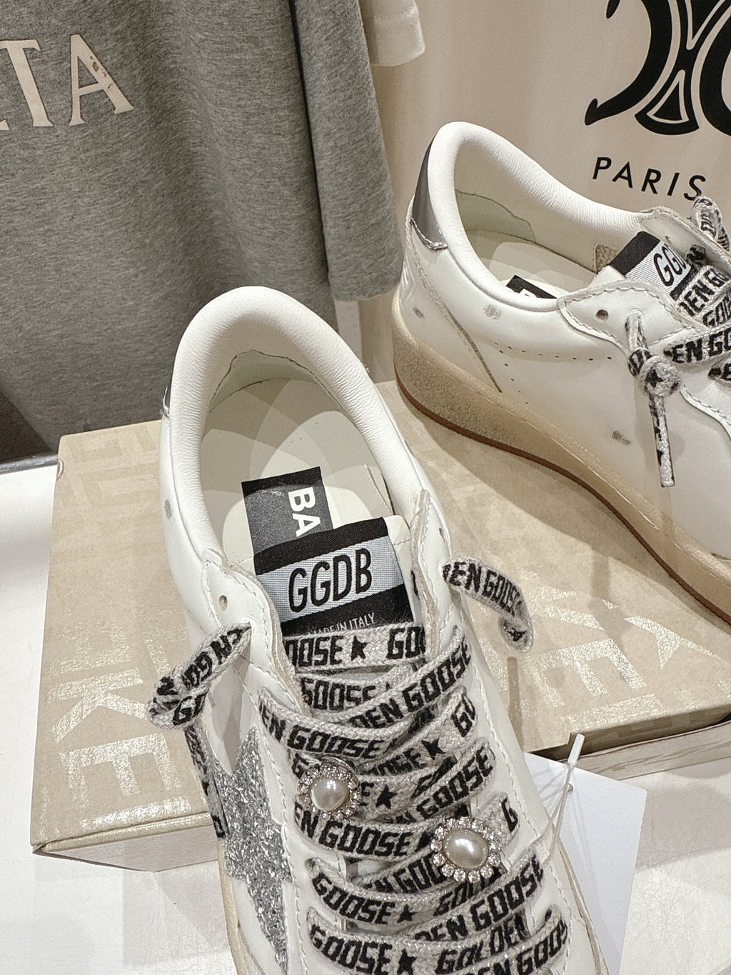 White low-top sneakers showing tongue label and black repeating text