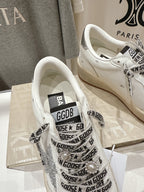 White low-top sneakers showing tongue label and black repeating text