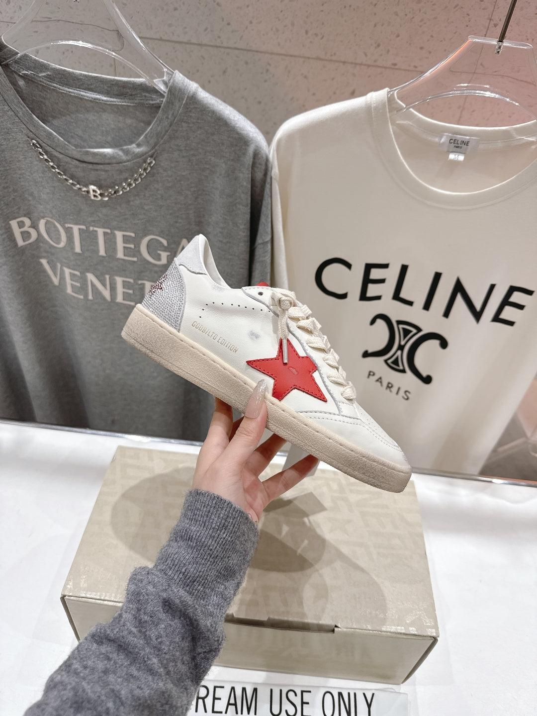 White lace-up low-top sneakers with red star patch on side, on display box