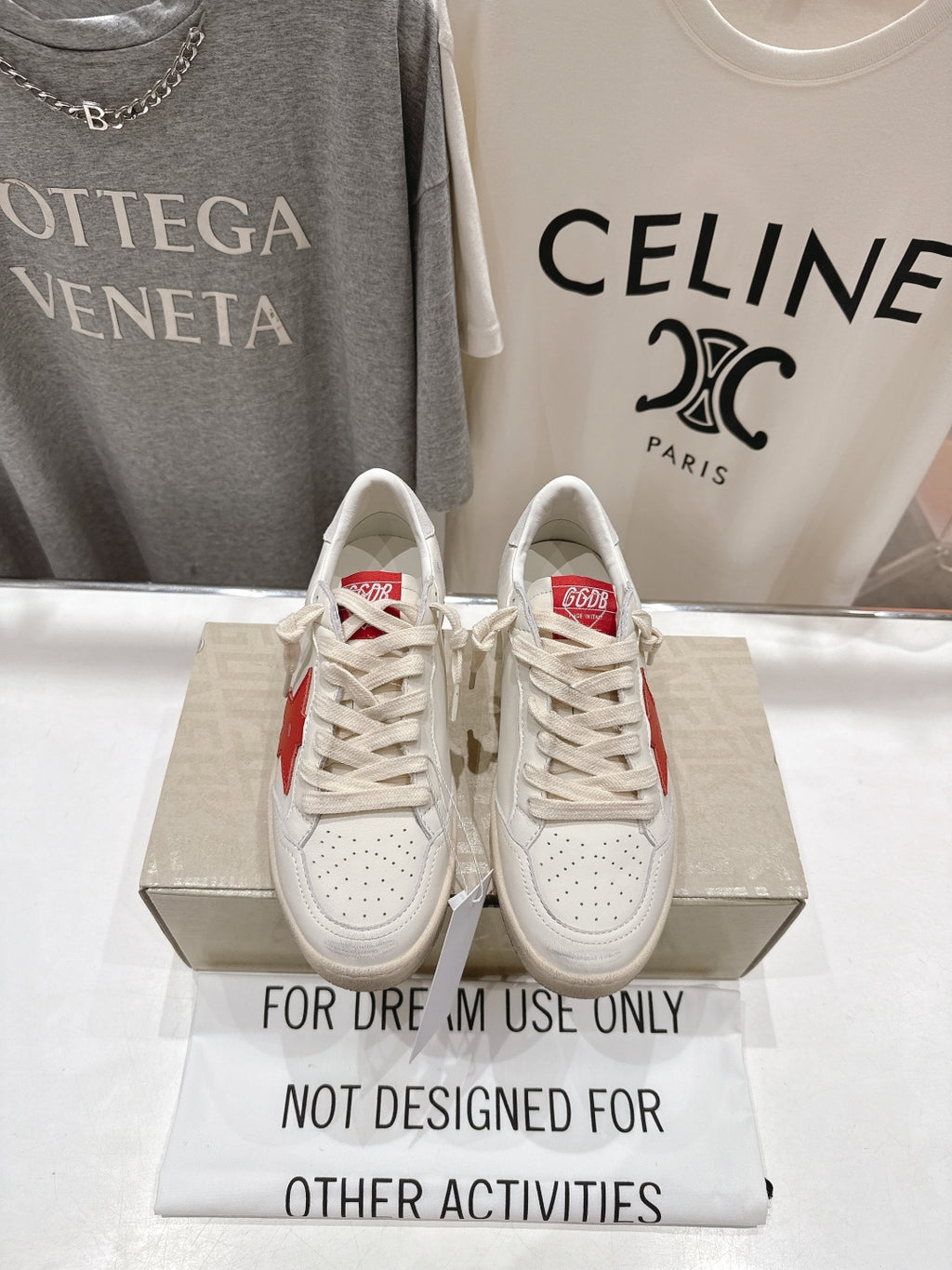 White lace-up low-top sneakers with perforated toe and red heel detail on display box