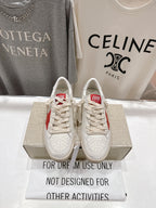White lace-up low-top sneakers with perforated toe and red heel detail on display box