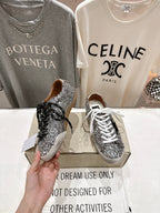 Hands holding silver sequin sneakers on box, black lace and white lace