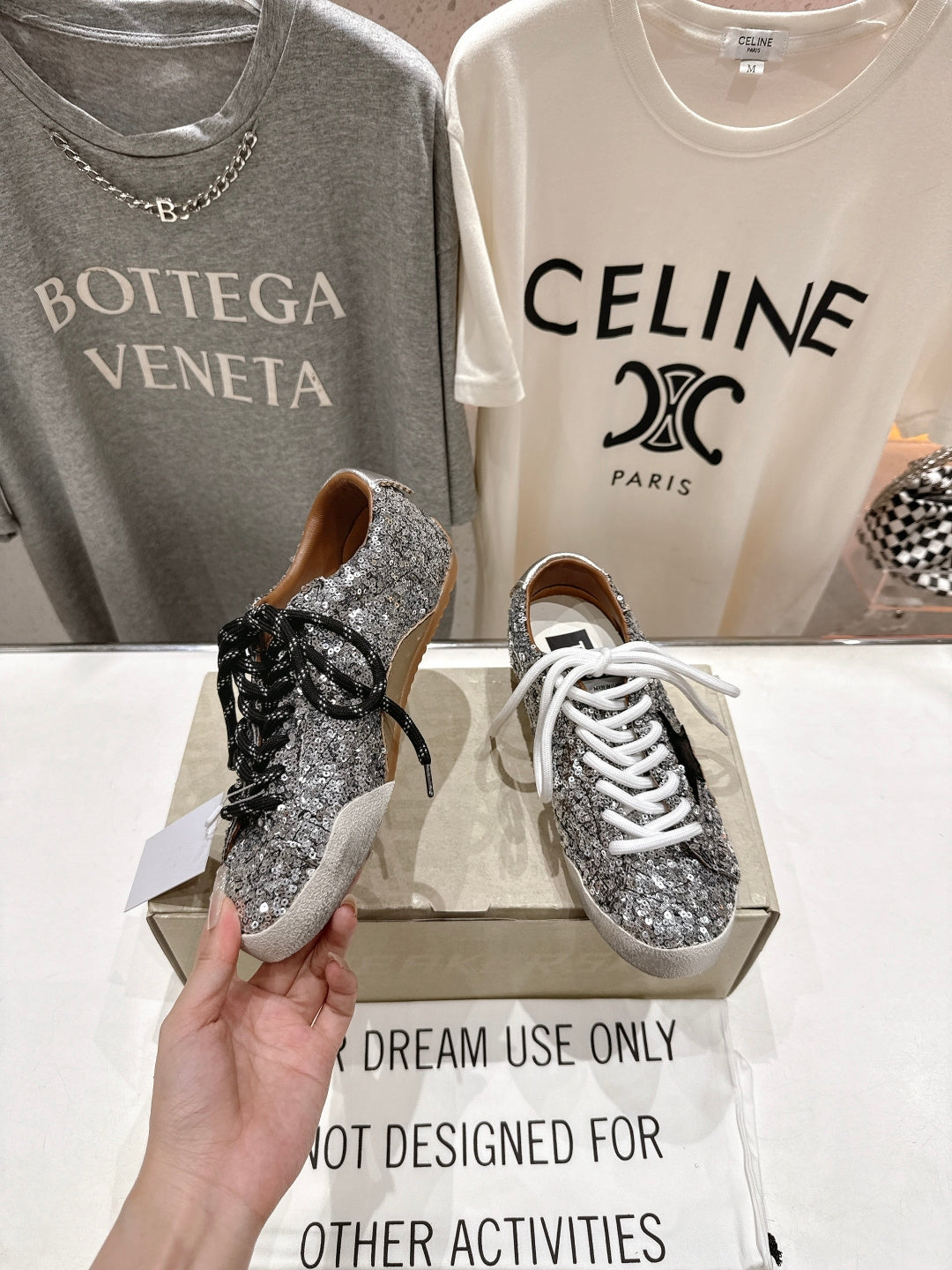 Hands holding silver sequin sneakers on box, black lace and white lace