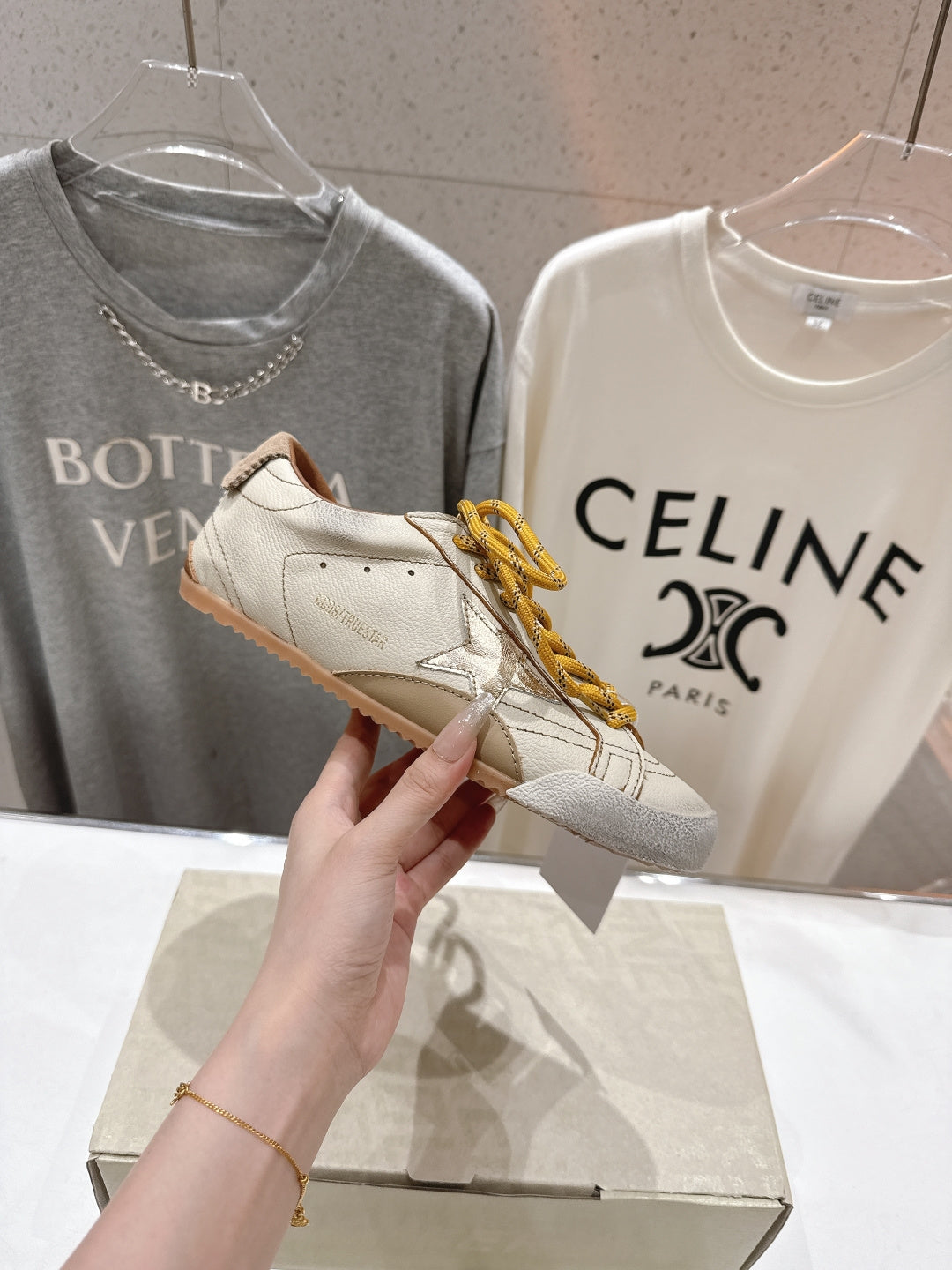 Golden Goose sneaker held in hand, white leather with yellow lace-up detail