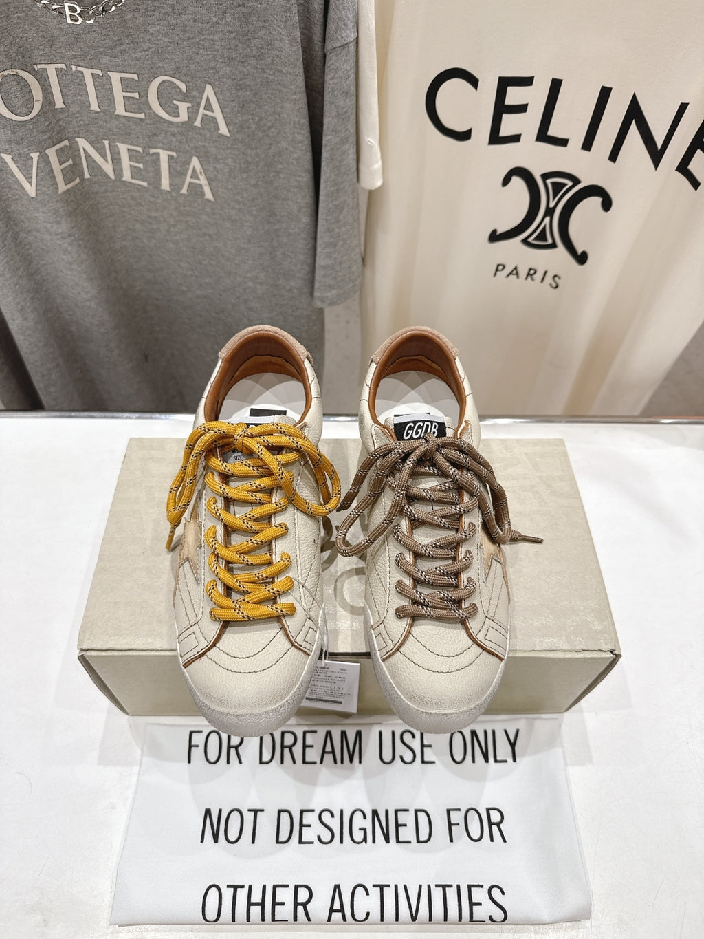 Golden Goose sneakers pair, white uppers with yellow and taupe laces on display box