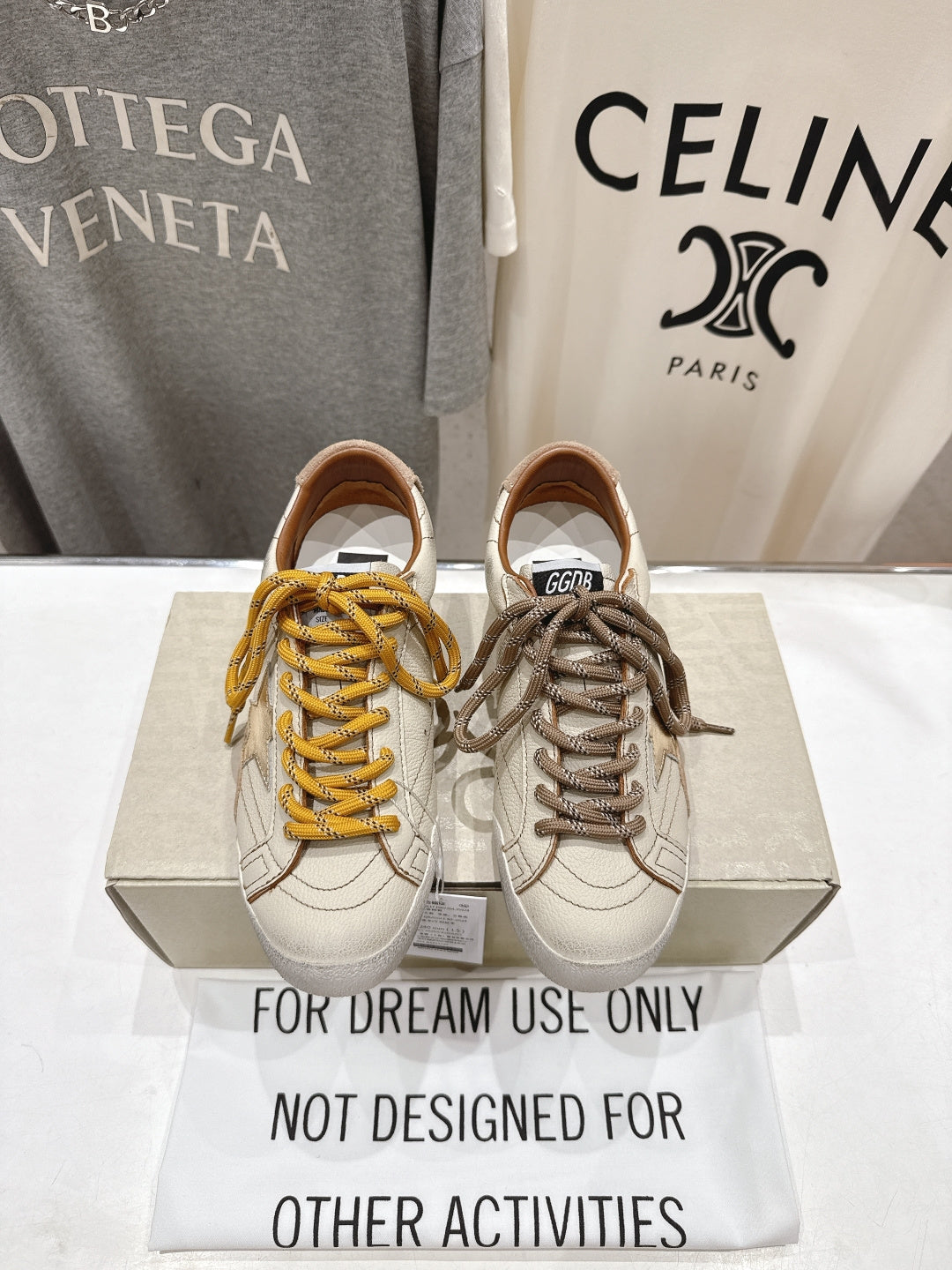 Golden Goose sneakers pair, white uppers with yellow and taupe laces on display box