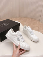 White Prada unisex sneakers held in hand, lace-up with logo patch