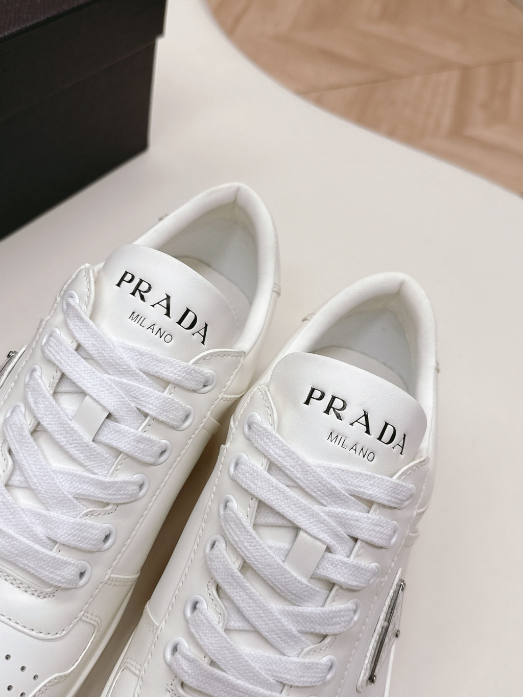 White Prada unisex sneakers close-up, PRADA Milano branding on tongues