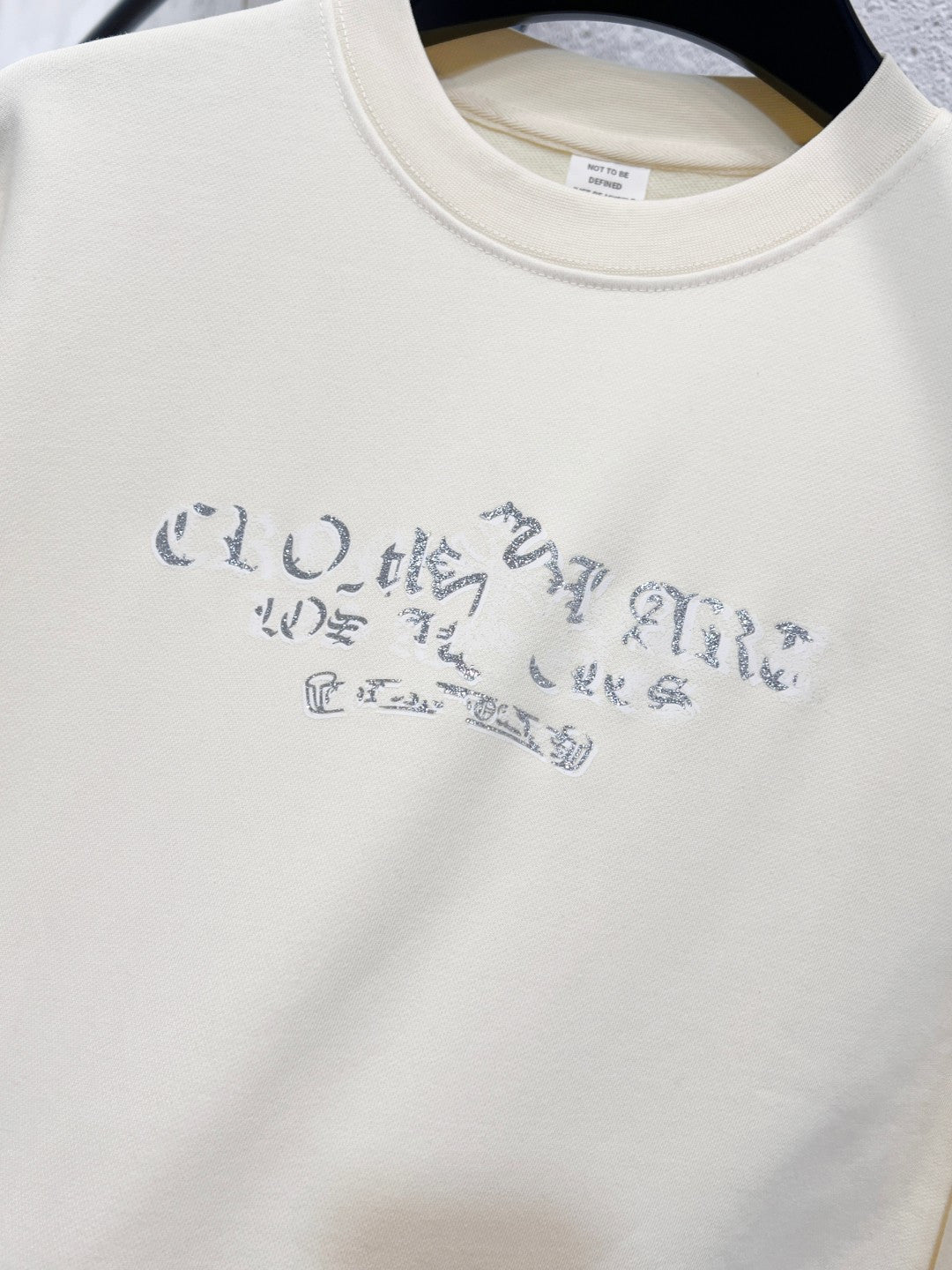 Close-up of blue graphic lettering centered on a cream sweatshirt front.