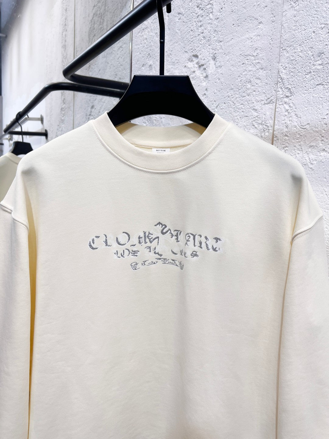 Cream long-sleeve crewneck sweatshirt with blue graphic lettering on chest.