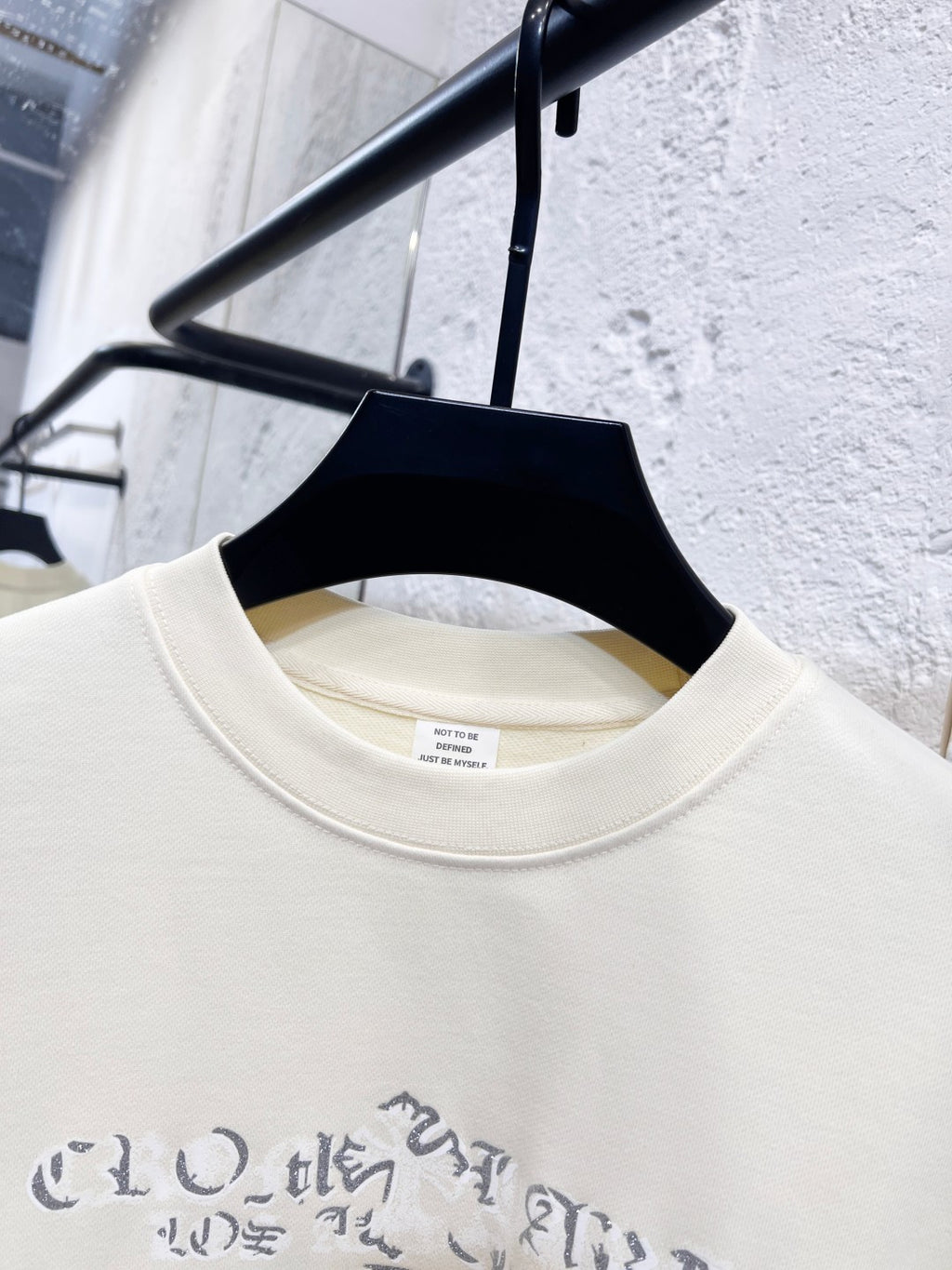Close-up of crewneck collar and blue graphic print on cream sweatshirt.