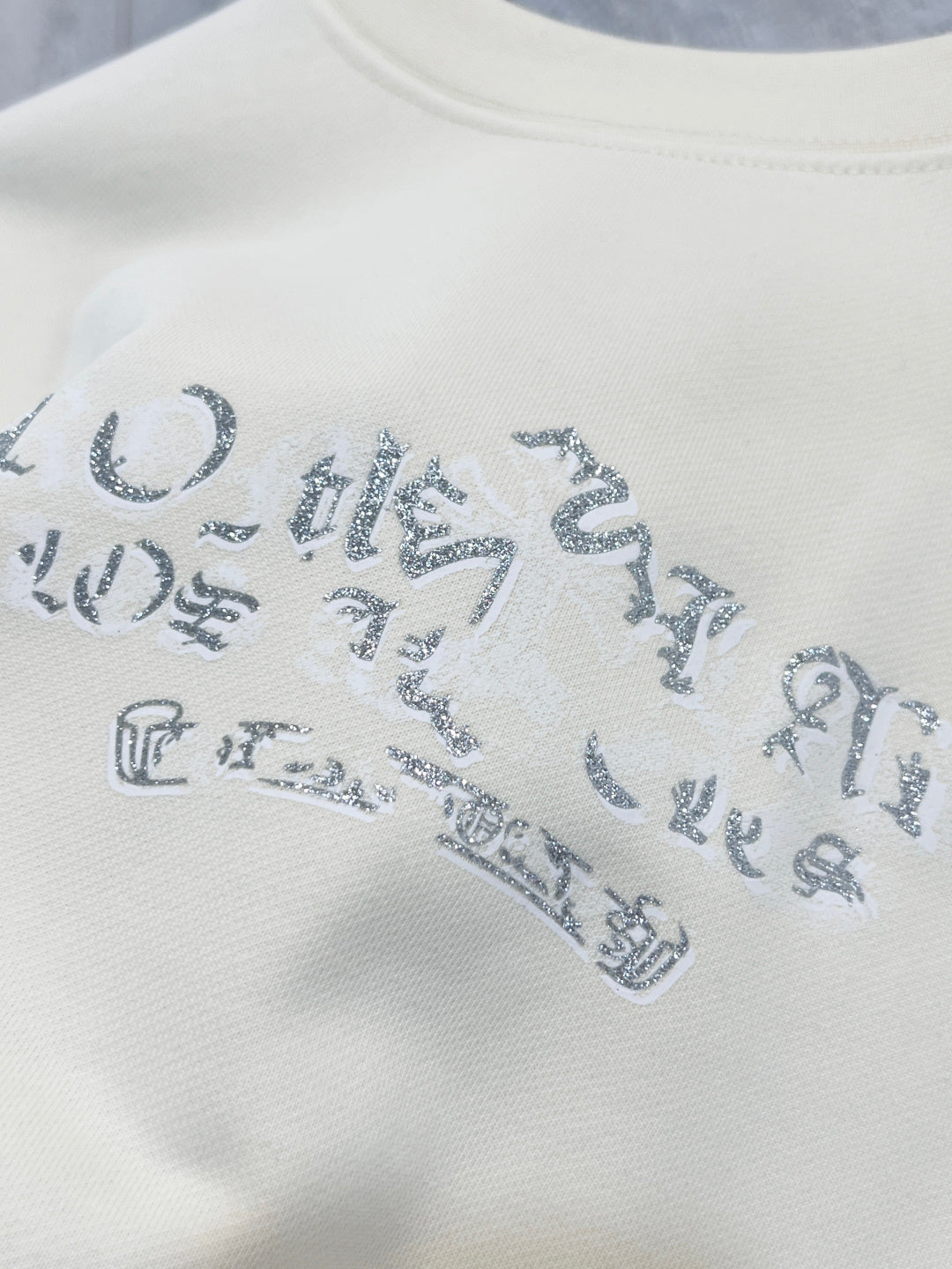 Close-up of blue graphic lettering on a cream sweatshirt front.