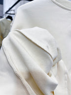 Cream sweatshirt sleeve and ribbed cuff detail with knit texture.