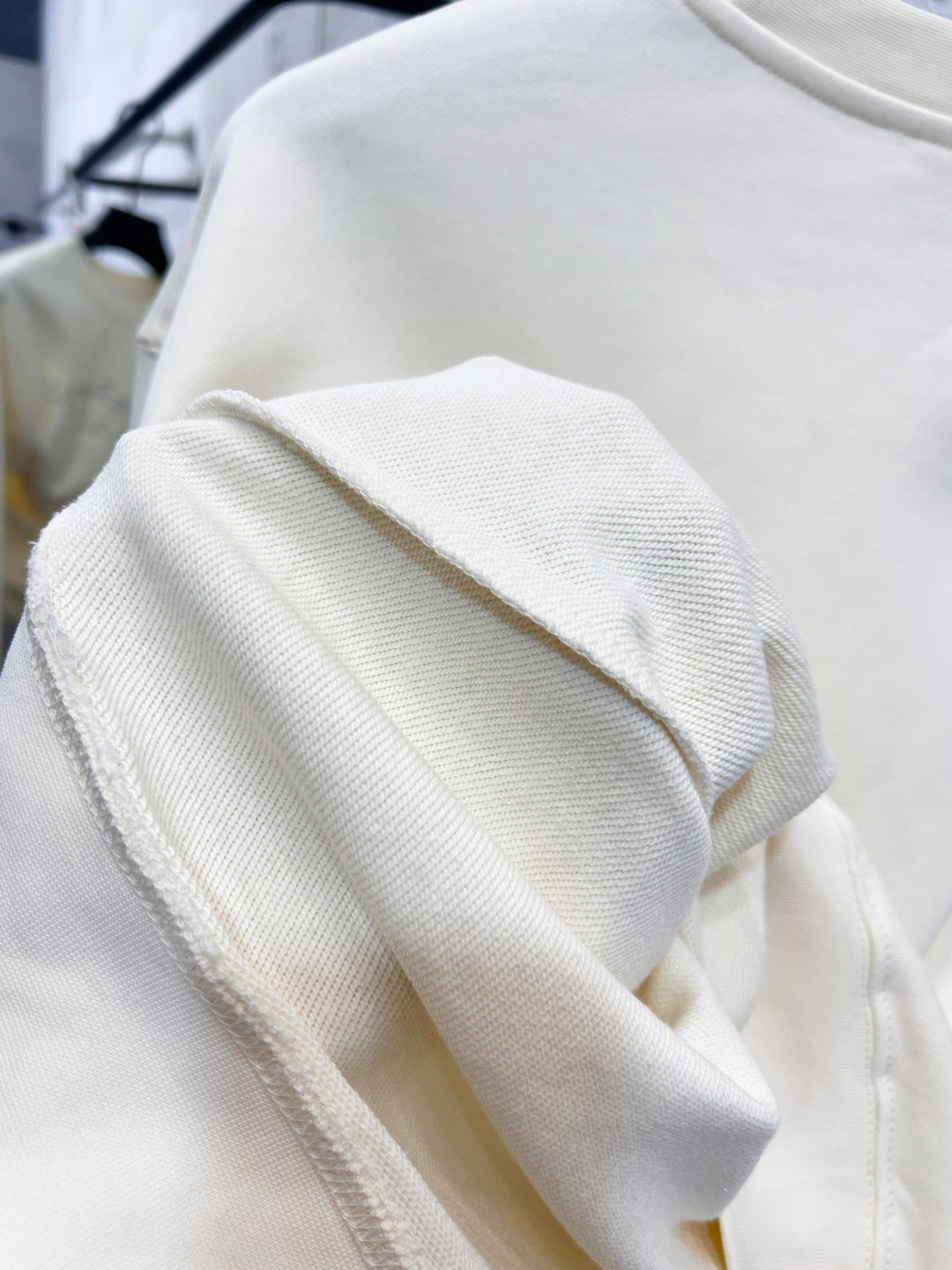 Cream sweatshirt sleeve and ribbed cuff detail with knit texture.