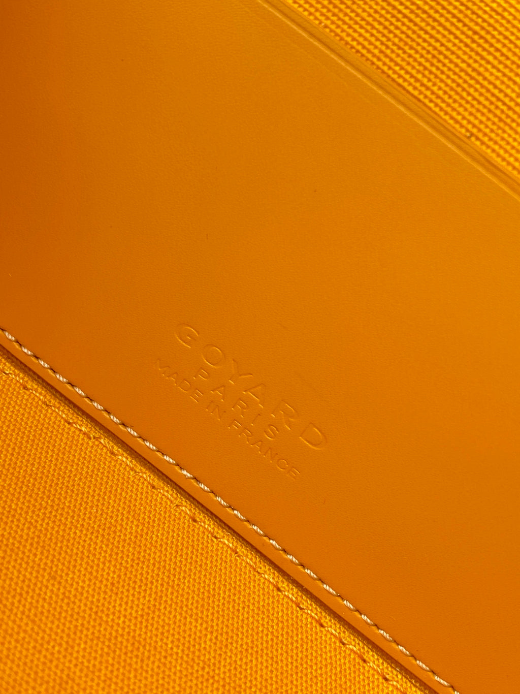 Yellow leather bag panel with embossed signature lettering and stitched edge