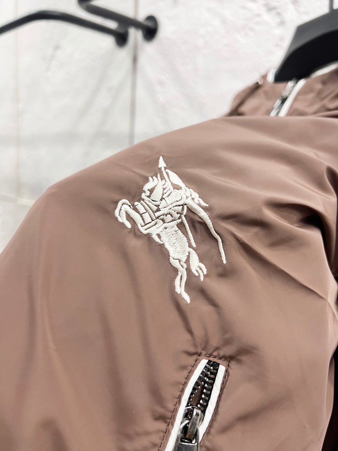 Taupe jacket shoulder with white horse logo patch and zip pocket