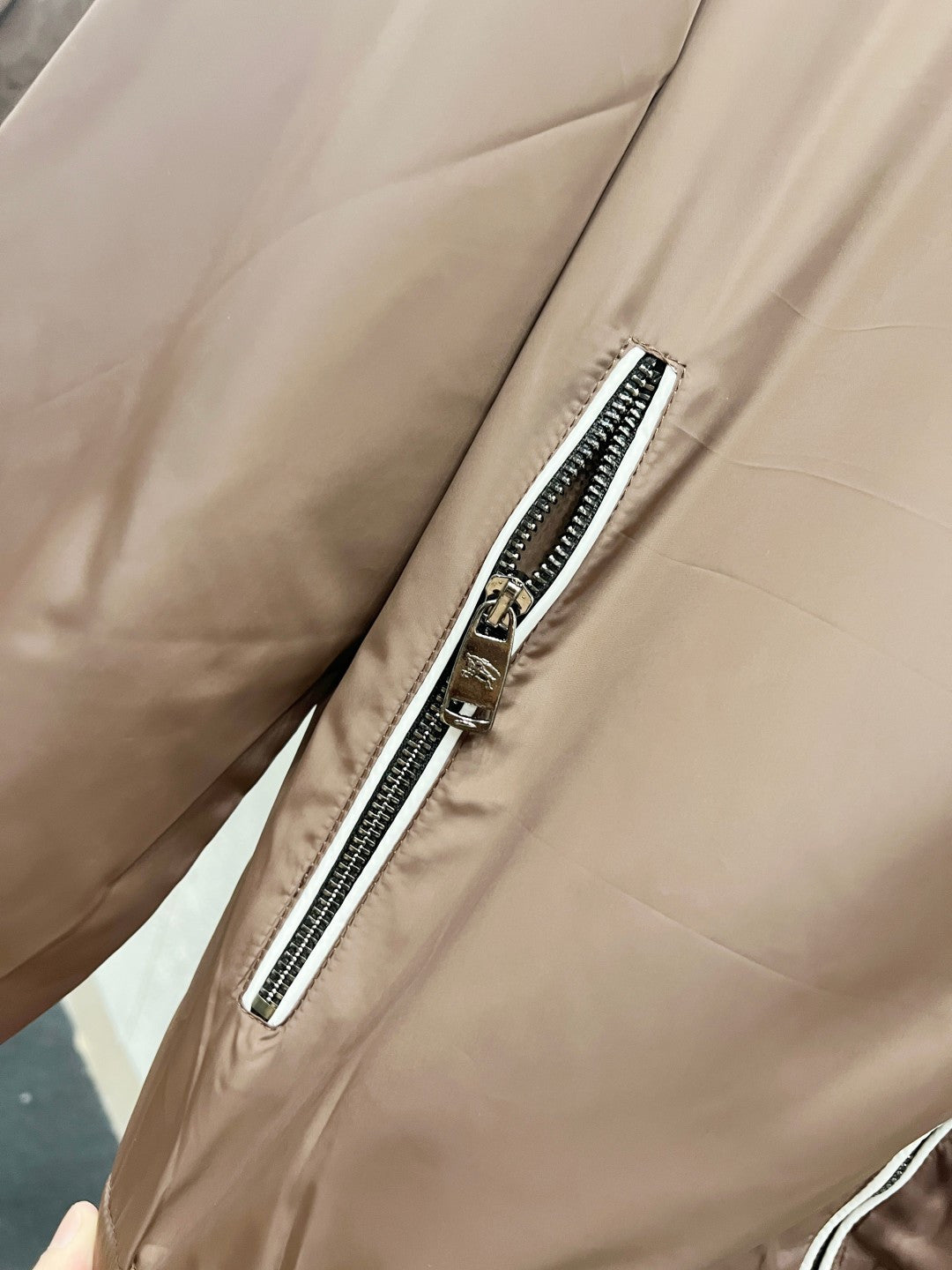 Close-up of taupe jacket with diagonal zip pocket and black-and-white trim