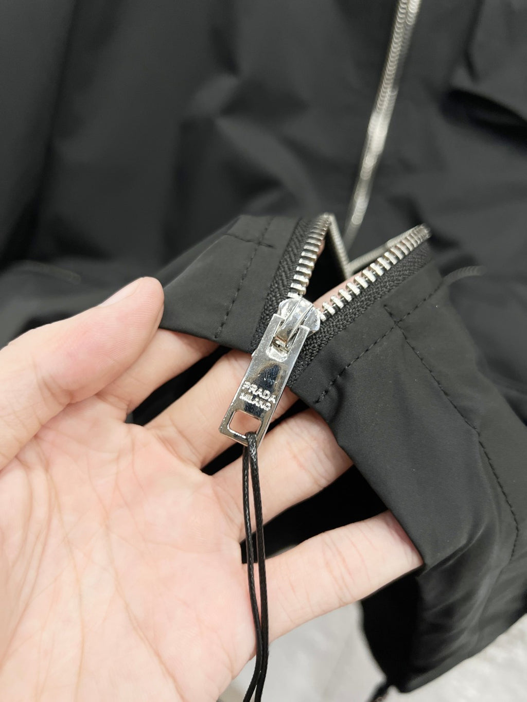 Prada jacket zipper and pull tab detail on black fabric
