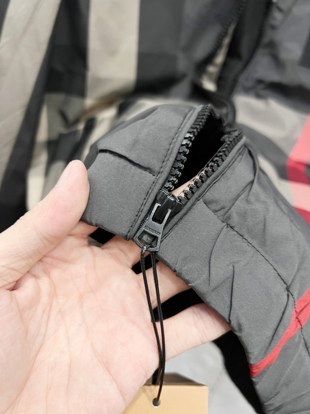 Burberry jacket sleeve cuff with zipper pocket detail in dark gray, close-up on hand