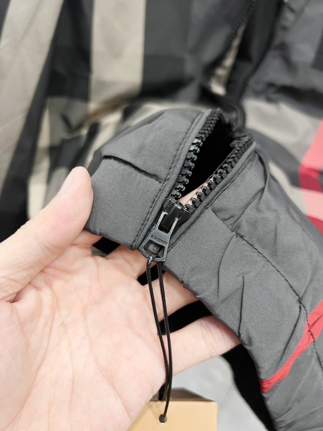 Burberry jacket sleeve cuff with zipper pocket detail in dark gray, close-up on hand