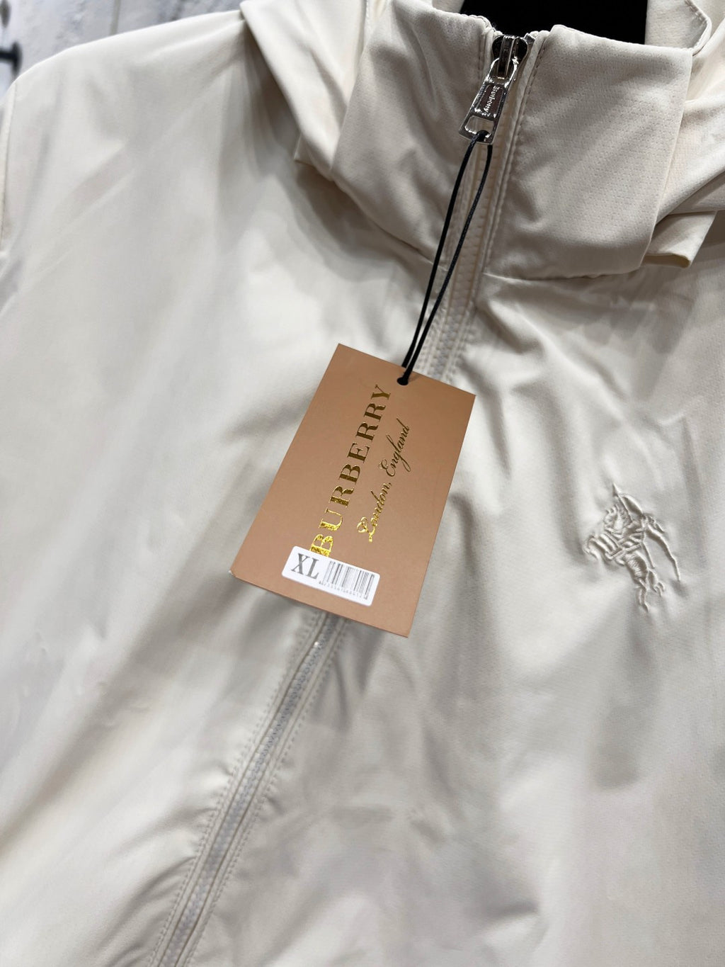 White hooded jacket close-up with front zipper, hanging brand tag, and small logo