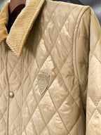 Light quilted jacket front close-up with small logo shield emblem and snap