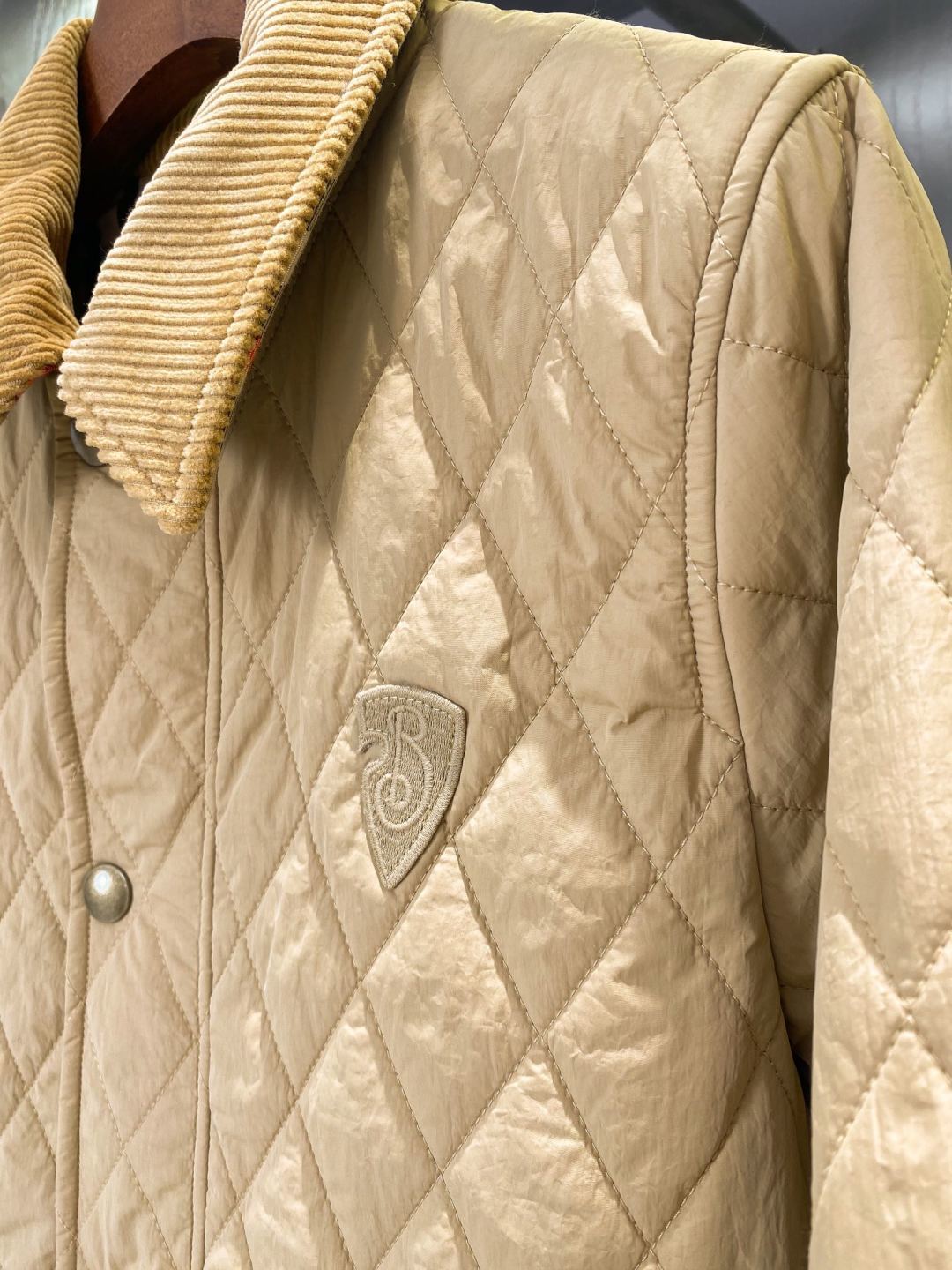 Light quilted jacket front close-up with small logo shield emblem and snap