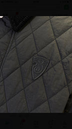 Quilted jacket fabric close-up with dark logo badge on the chest