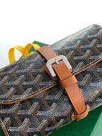Goyard bag close-up: dark monogram canvas, tan leather strap, metal buckle