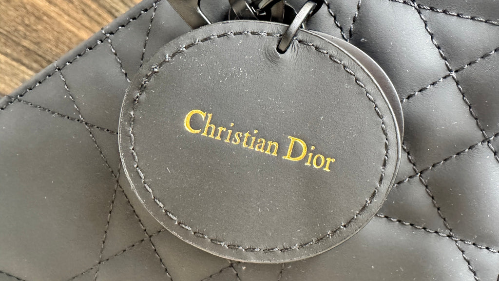 Dior round logo charm with “Christian Dior” text on dark gray quilted bag