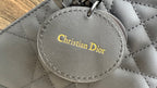 Dior round logo charm with “Christian Dior” text on dark gray quilted bag