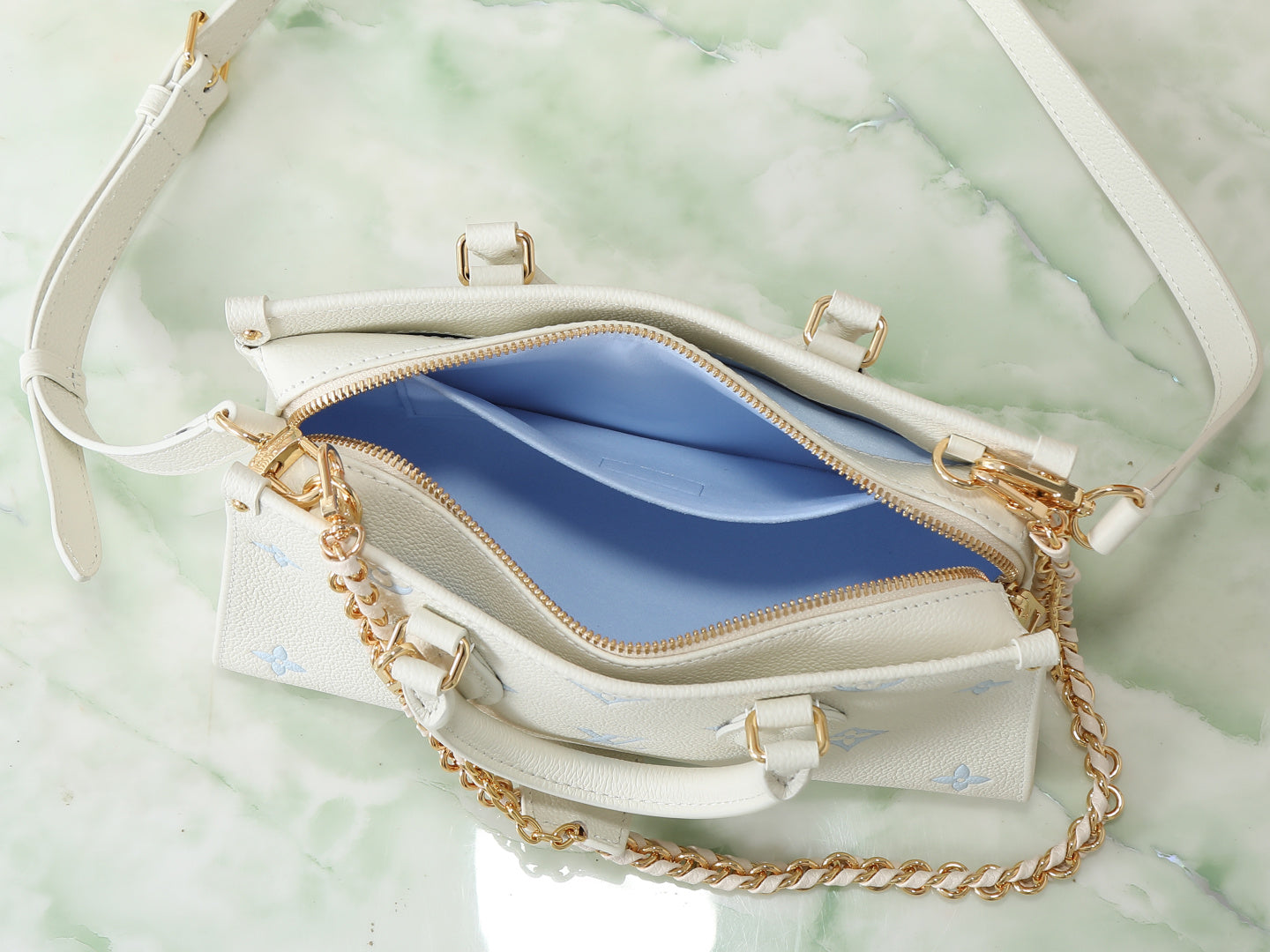 Louis Vuitton bag open view with white exterior, blue fabric lining, and gold hardware