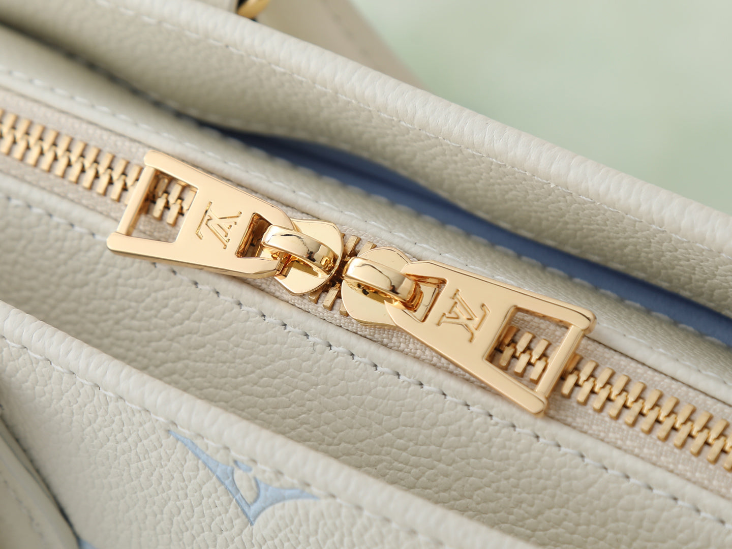 Louis Vuitton bag zipper close-up with gold pull and light blue monogram on white leather