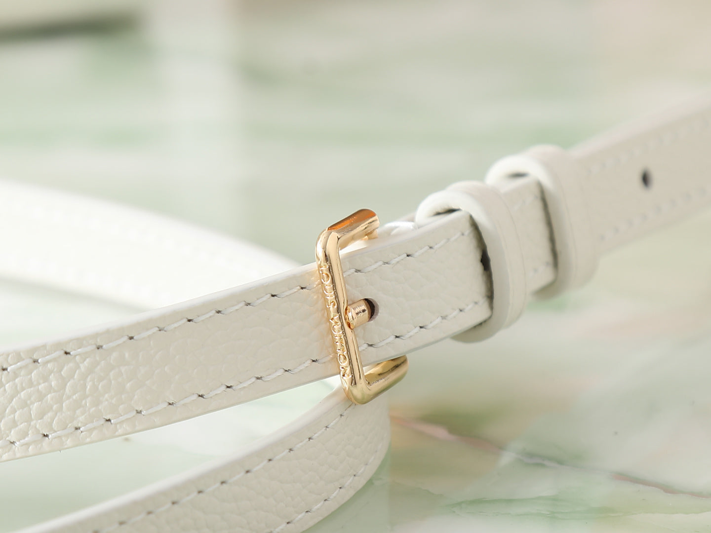 Louis Vuitton bag strap detail with gold-tone buckle on white leather