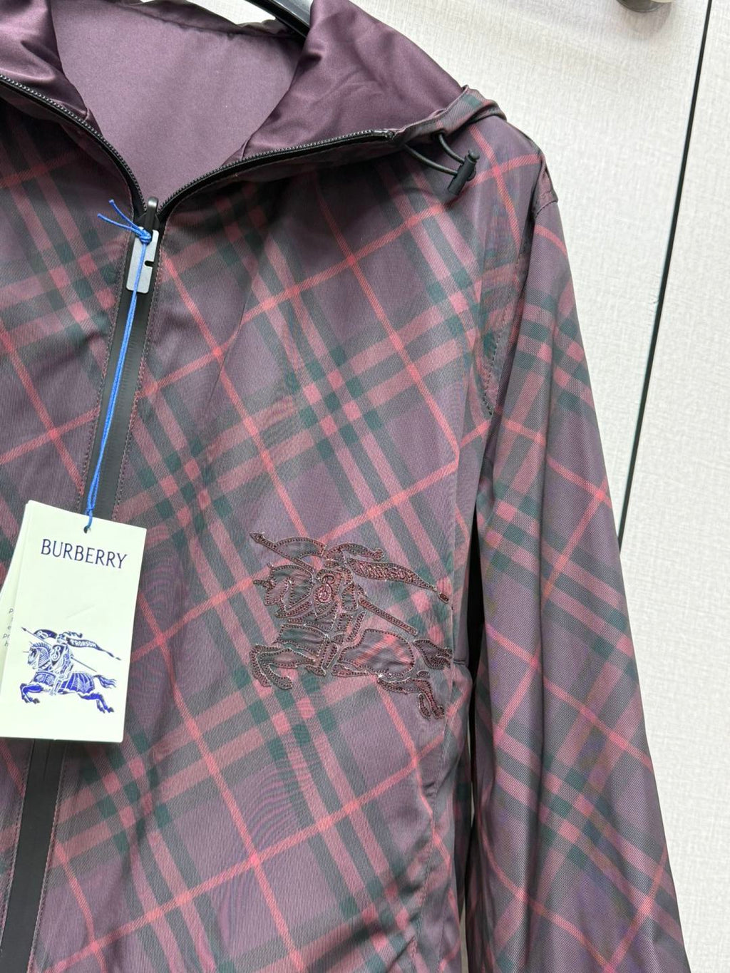 Burberry plaid hooded jacket with embroidered crest detail and zip placket.